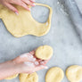 Hands shaping dough rounds for DIY jelly doughnut kit on marble surface with rolling pin nearby
