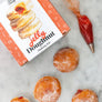 DIY jelly doughnut kit by Farm Steady with doughnuts and piping bag filled with jelly on marble surface