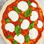 Unbaked margherita pizza with tomato sauce, fresh mozzarella, and basil leaves from margherita pizza making kit