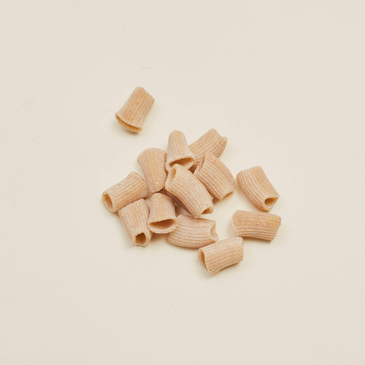 A small pile of dry penne pasta pieces on a plain warm off-white background.