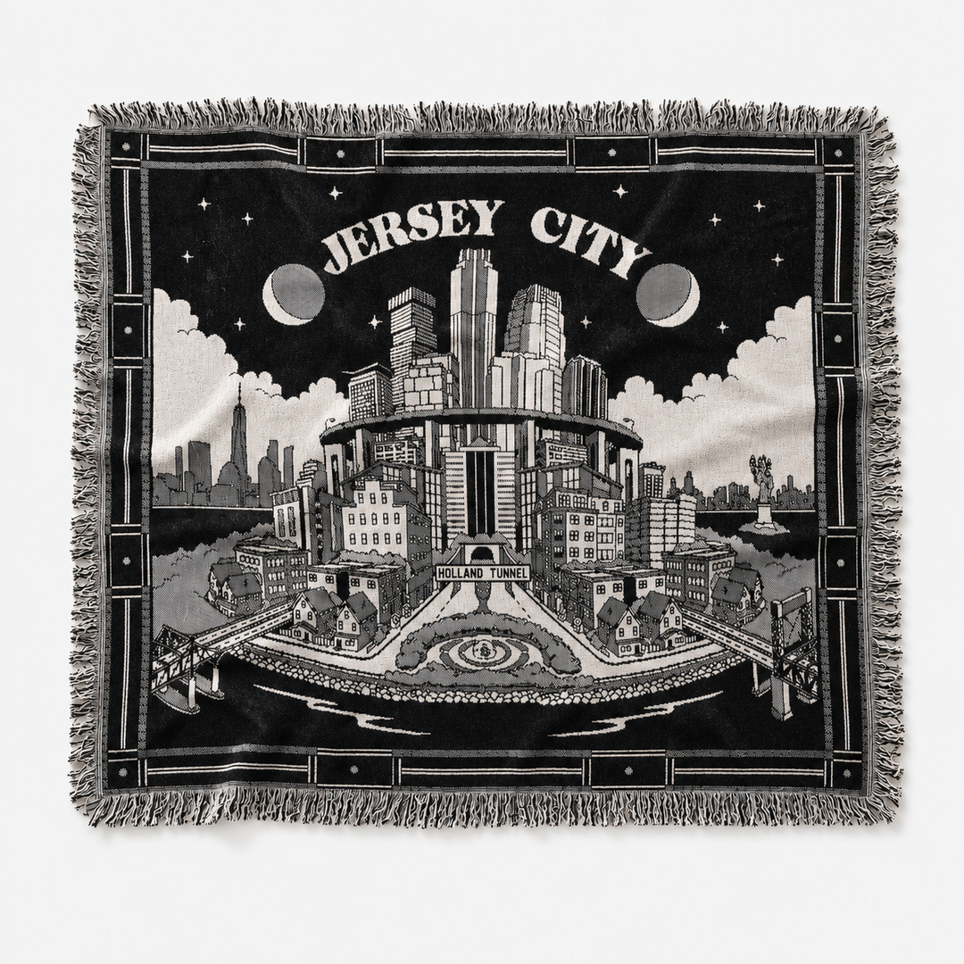 Woven blanket with a black and white illustration of Jersey City, featuring buildings and text.