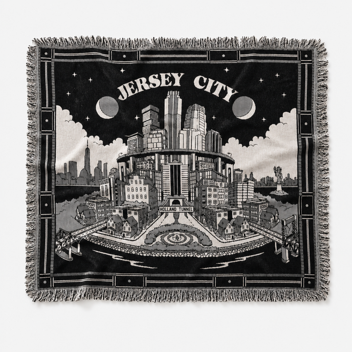 Woven blanket with a black and white illustration of Jersey City, featuring buildings and text.