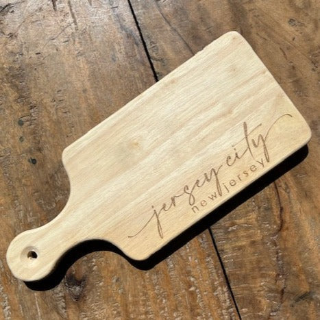 Rectangular cutting board with a handle that reads "Jersey City, New Jersey" 