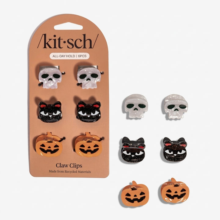 Six Halloween-themed claw clips by kit·sch, shown both on their tan retail card and loose beside it. The set includes skull, black cat, and orange pumpkin designs in glossy and glitter finishes.