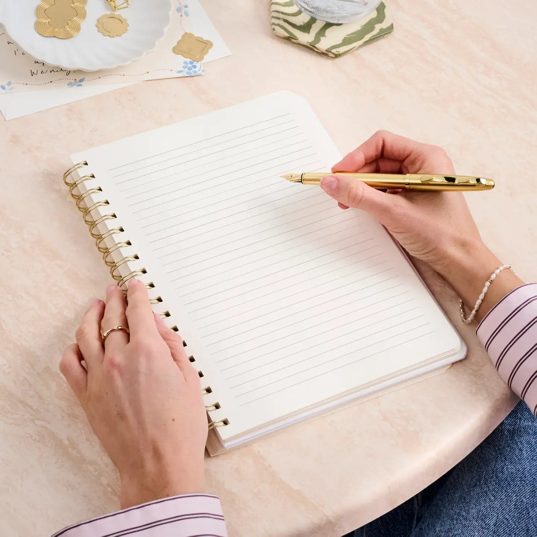 B5 hardcover spiral notebook with blank lined pages and a gold pen ready for writing