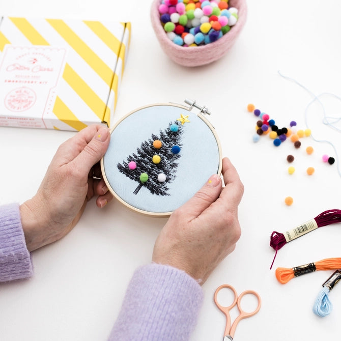 Christmas Craft Kit hands holding Cotton Clara embroidery hoop with stitched tree and colorful pom pom ornaments