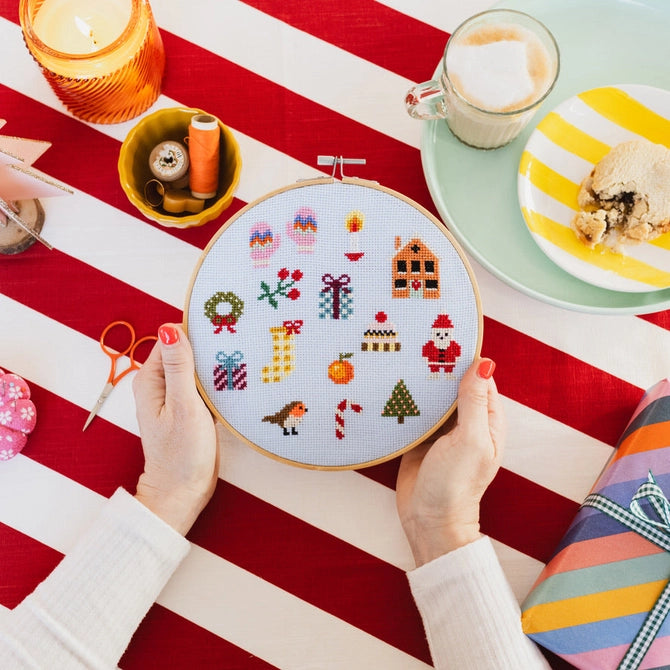 Cotton Clara Craft kit Christmas cross stitch hoop with festive icons held over red striped tablecloth