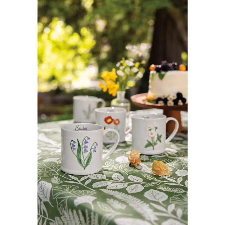 Danica embossed daisy mug showcased on a green table with floral patterns and a cake in the background