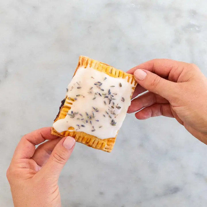 Hands holding a freshly made pastry tart from the pastry tart DIY kit with icing and lavender