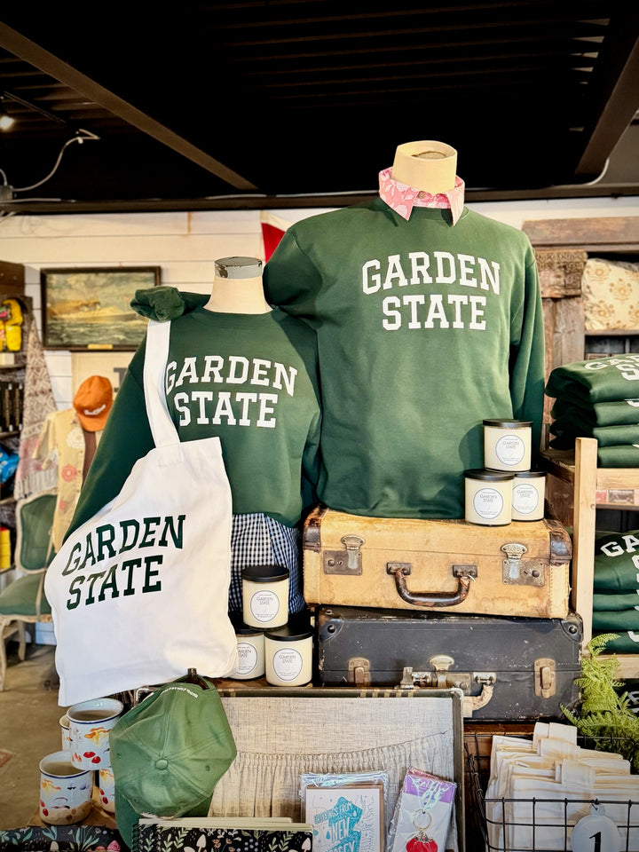Kanibal & Co. Garden State sweatshirt displayed on mannequins with matching tote bag and stacked vintage suitcases