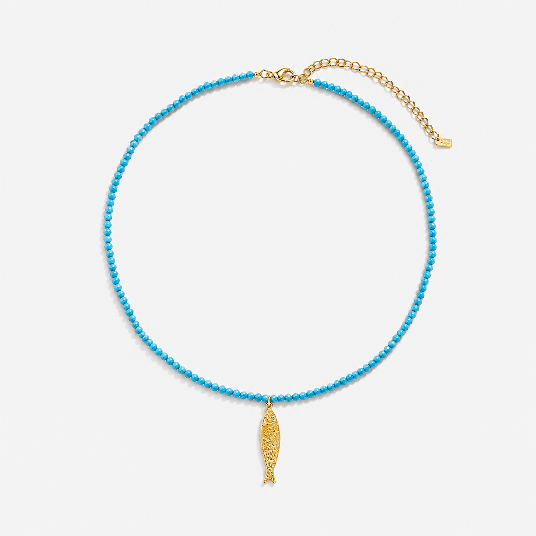 Blue beaded necklace with a gold fish pendant on a light gray background