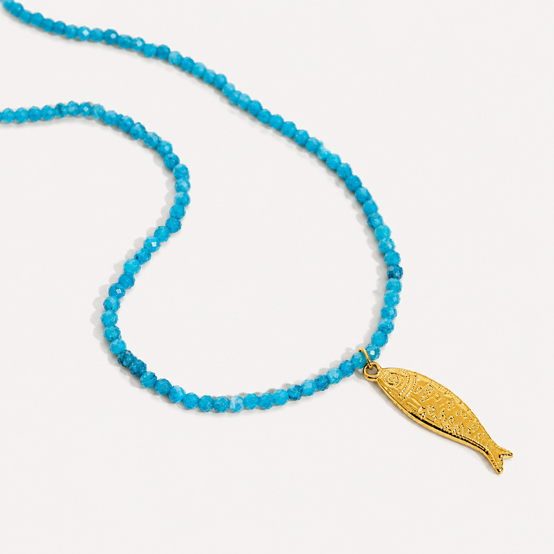 Blue beaded necklace with a gold fish pendant on a white background