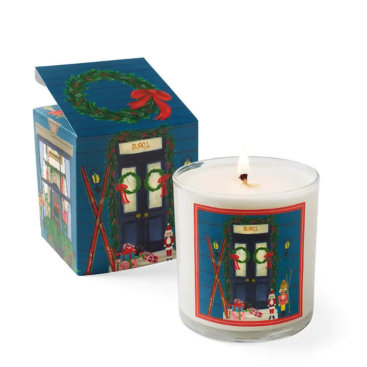 Home for the holidays candle in festive packaging featuring a decorated door and winter decorations