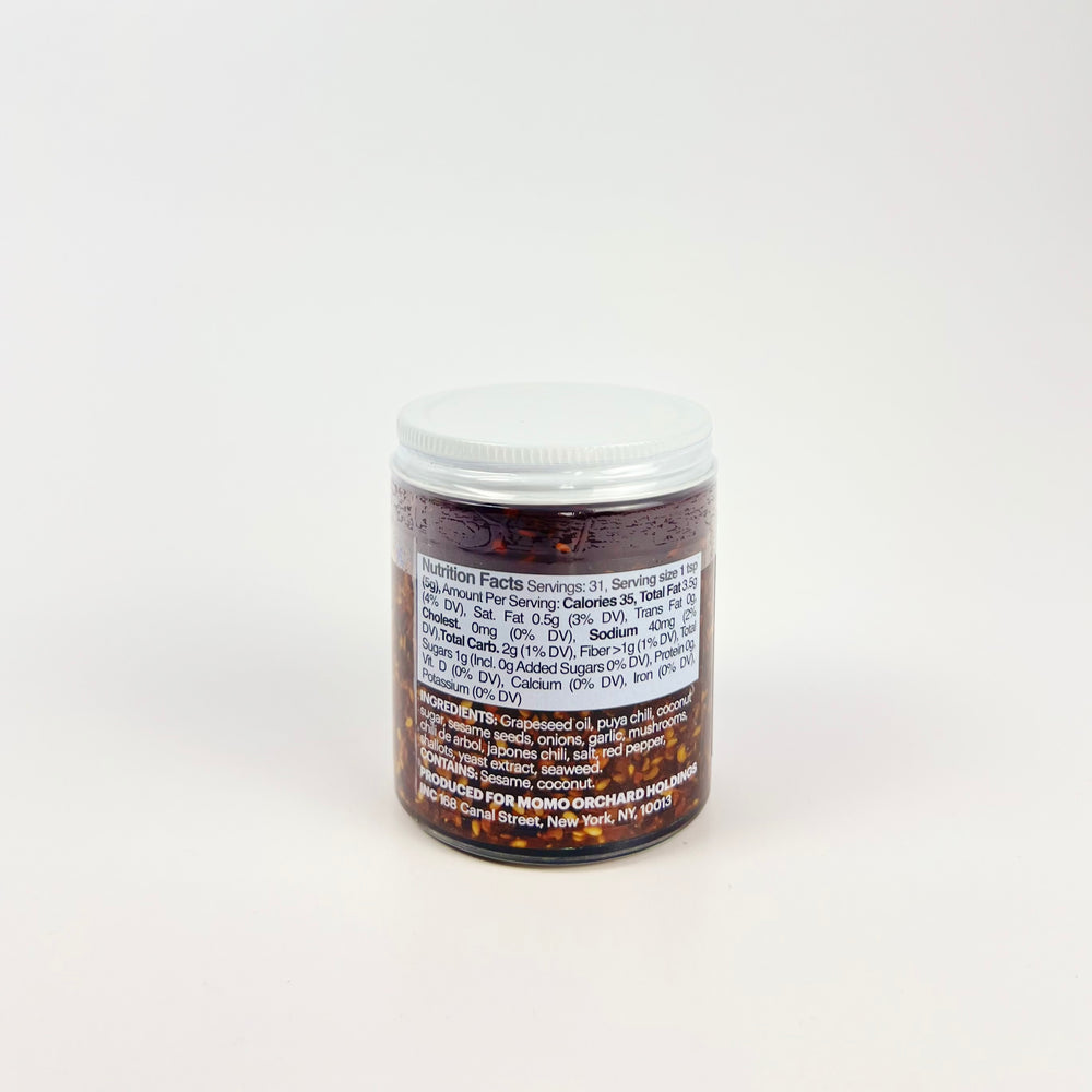 Glass jar of Momofuku Chili Crunch showing nutrition label and chili oil flakes