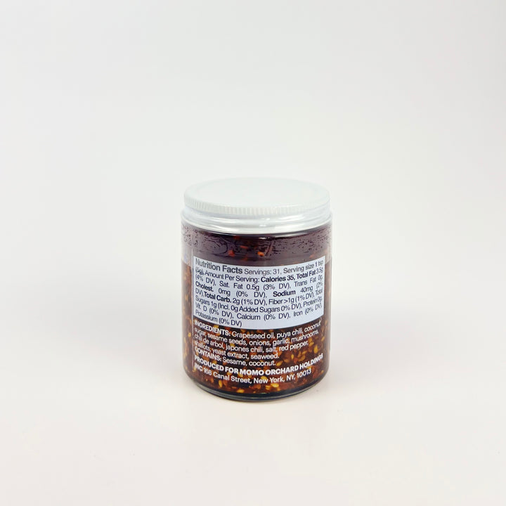 Glass jar of Momofuku Chili Crunch showing nutrition label and chili oil flakes
