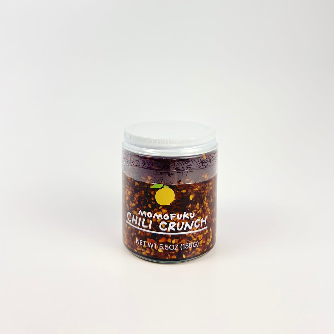 Jar of Momofuku Chili Crunch pantry condiment in clear jar with white lid showing chili flakes and oil