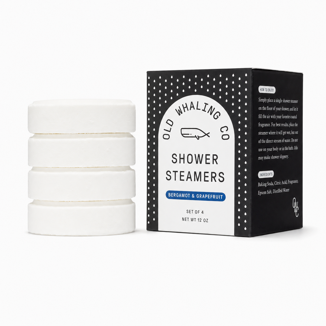A set of four white round shower steamer discs stacked on the left, next to their black and white packaging box by Old Whaling Co. on a clean white background.