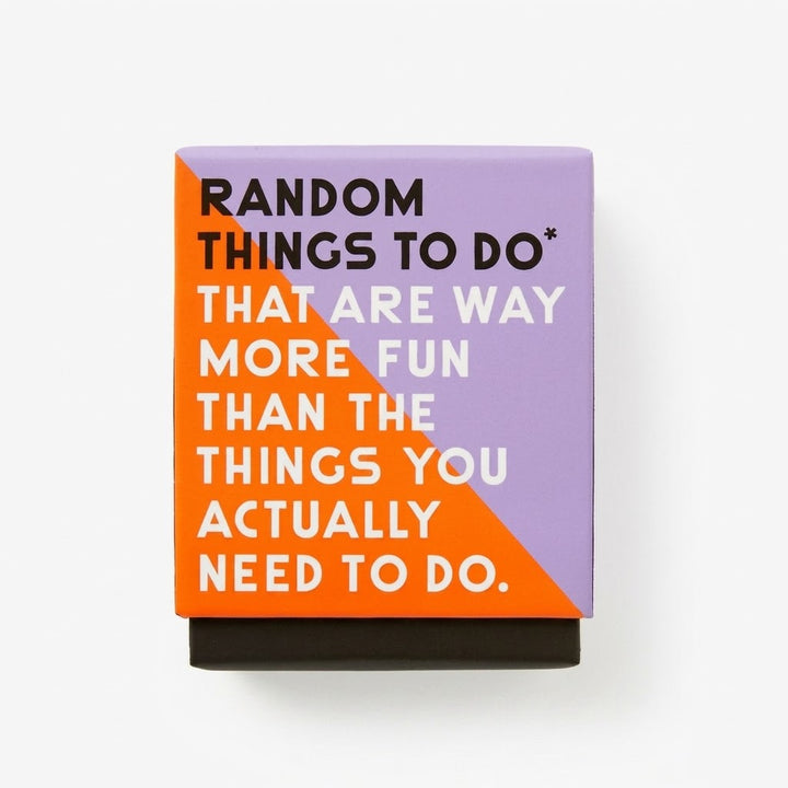 A square decorative block or plaque with a typographic design, featuring the quote 'RANDOM THINGS TO DO* THAT ARE WAY MORE FUN THAN THE THINGS YOU ACTUALLY NEED TO DO.' in black and white text over a split orange and lavender background, with a black base, shown on a clean white background.