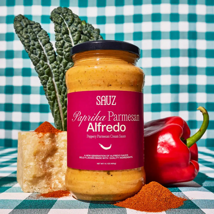 Sauz Paprika Parmesan Alfredo Sauce in a jar with red and green ingredients on a checkered background