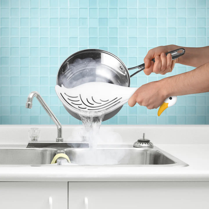 Fred & Friends silly goose pot strainer in use, draining pasta into a sink with steam rising
