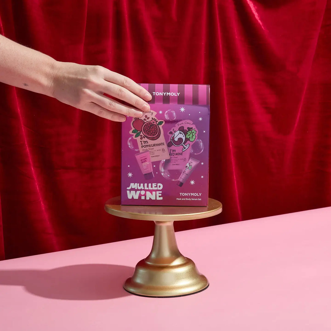 TonyMoly Mulled Wine Face and Body Set displayed on a golden pedestal with a hand reaching for it