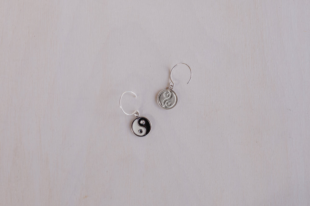 2 earrings one front facing with black and white yin yang and one showing silver back with yin yang 