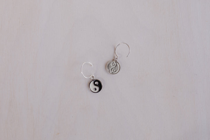 2 earrings one front facing with black and white yin yang and one showing silver back with yin yang 