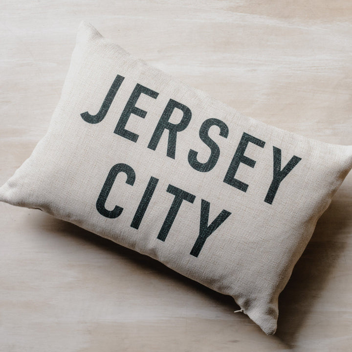 small rectangular cream pillow that reads Jersey City in black letters