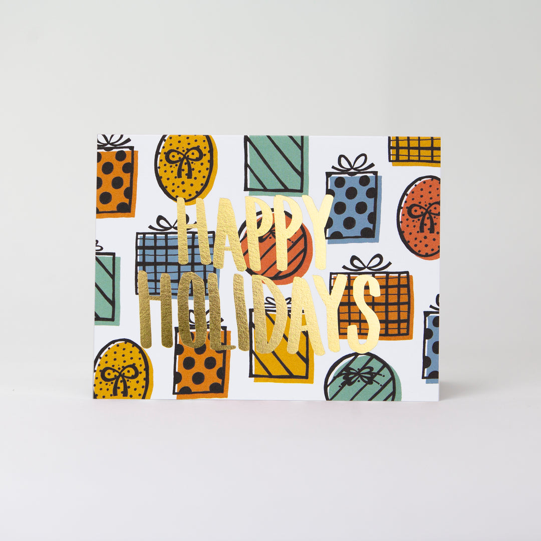 Gold foil HAPPY HOLIDAYS greeting card with illustrated presents in the background. Card is in a landscape layout
