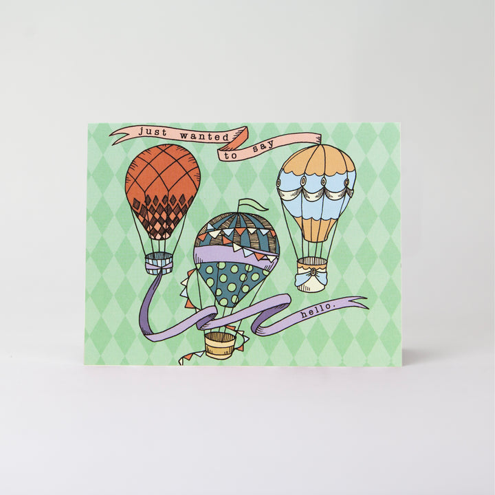 Rectangular card with a mint green background that reads "Just wanted to say hello" with illustrations of 3 multi colored hot air balloons. The card has a landscape layout
