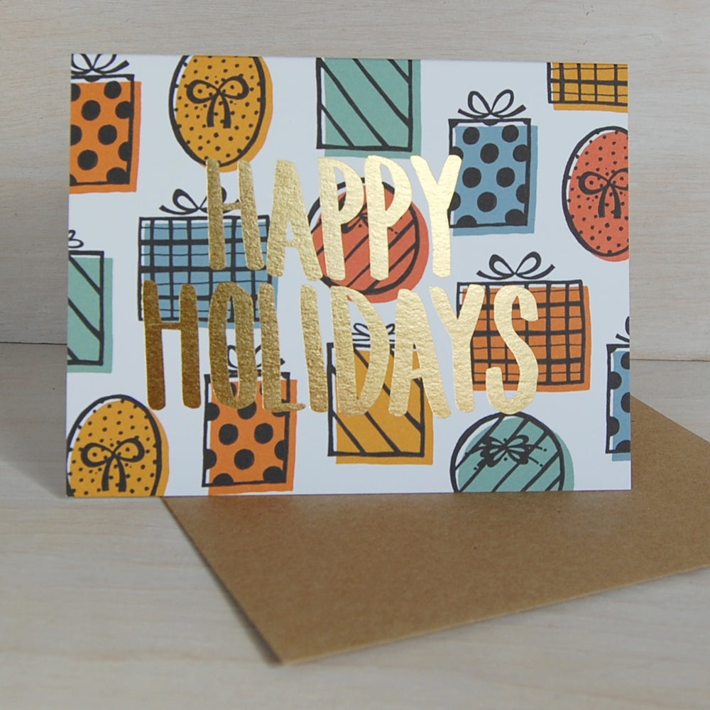 Gold foil HAPPY HOLIDAYS greeting card with illustrated presents in the background. Card is in a landscape layout