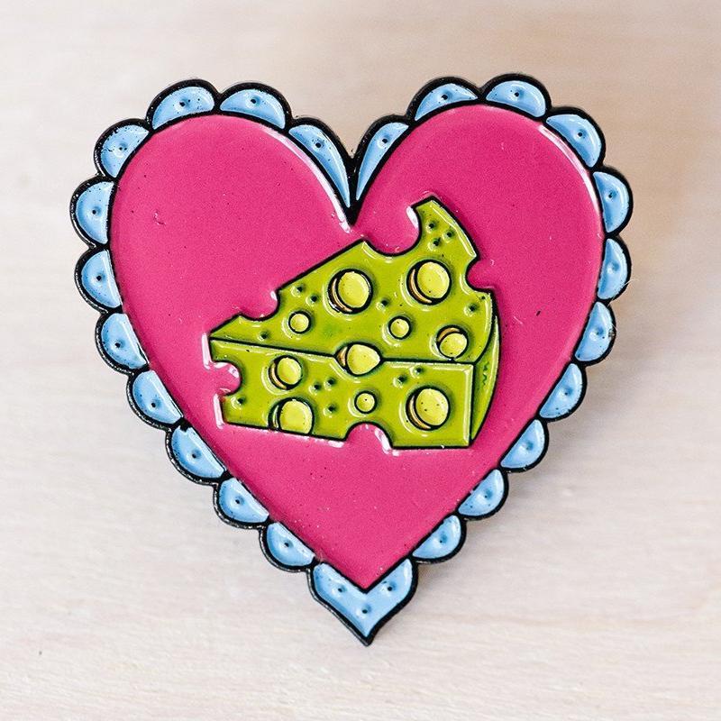 pink heart shaped pin with piece of yellow cheese in center and scalloped blue edges