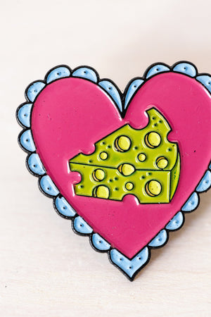 pink heart shaped pin with piece of yellow cheese in center and scalloped blue edges