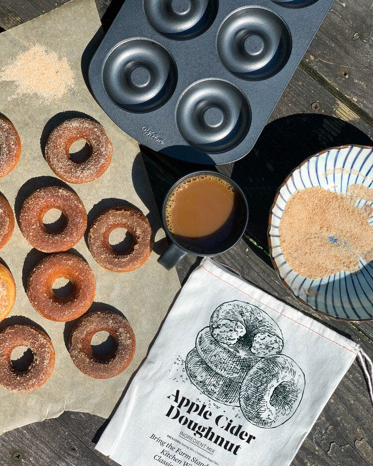 Apple cider doughnut baking kit with baked doughnuts, cinnamon sugar, and coffee on a rustic table
