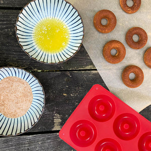 rectangular silicon baking pan with 6 donuts next to it and two bowls of baking ingredients