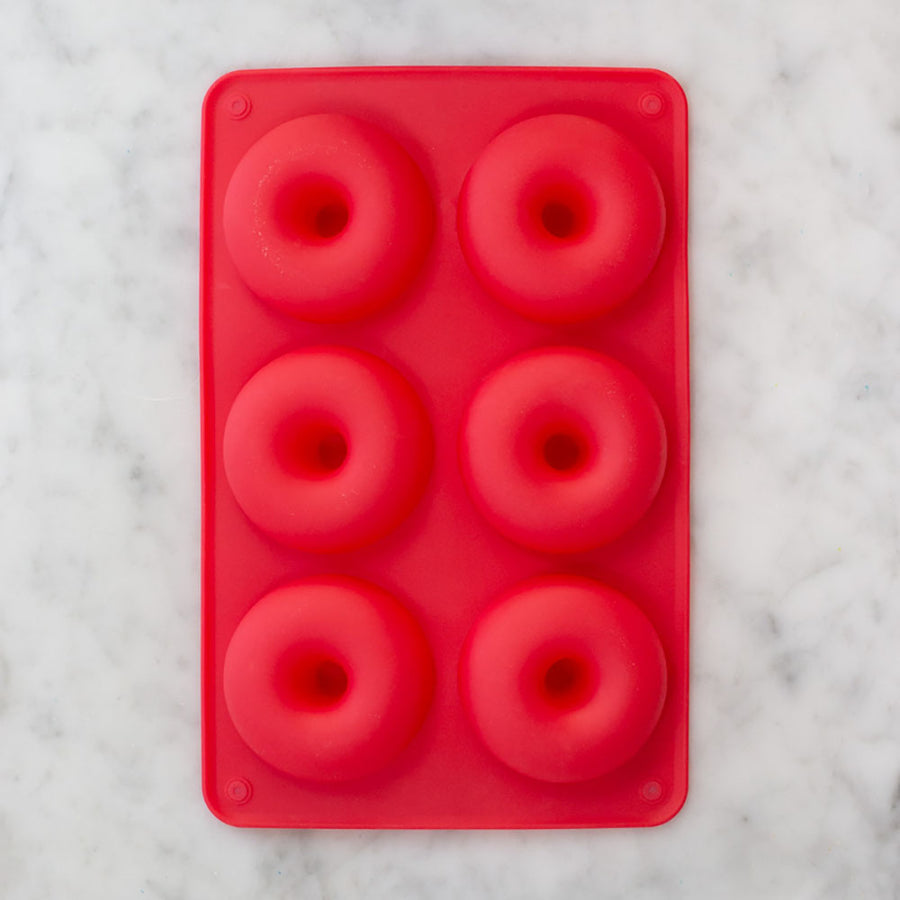 A red rectangular baking pan with 6 round indentations for donuts