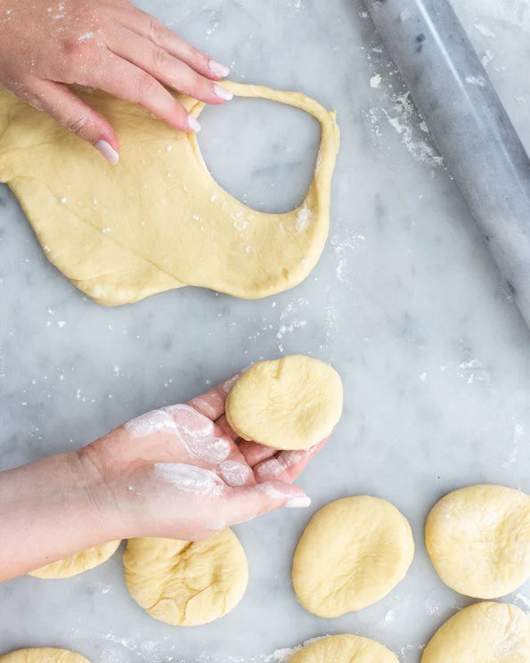 Hands shaping dough rounds for DIY jelly doughnut kit on marble surface with rolling pin nearby