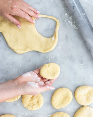 Hands shaping dough rounds for DIY jelly doughnut kit on marble surface with rolling pin nearby