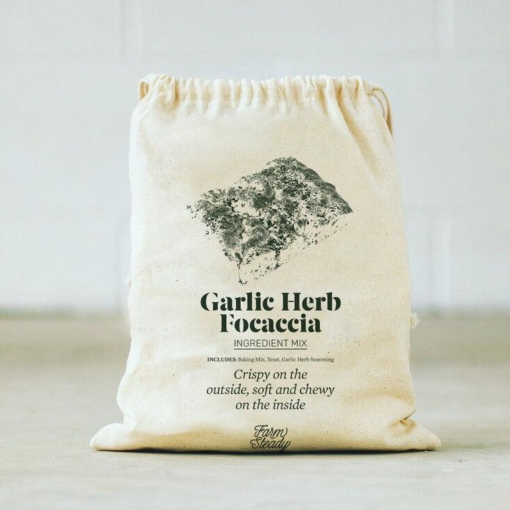 Farm Steady garlic herb focaccia baking kit in a beige drawstring bag with ingredient mix and seasoning