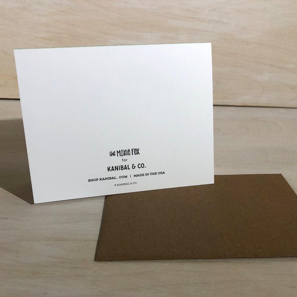 Back view of Kanibal & Co hot air balloon greeting card with brown envelope on wooden surface