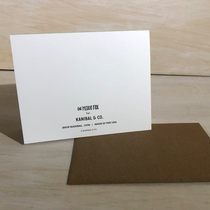Back view of Kanibal & Co hot air balloon greeting card with brown envelope on wooden surface
