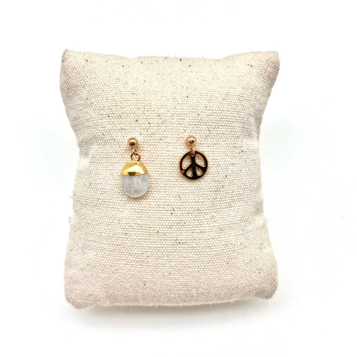 2 earrings on a cushion, one crystal drop, one peace sign charm