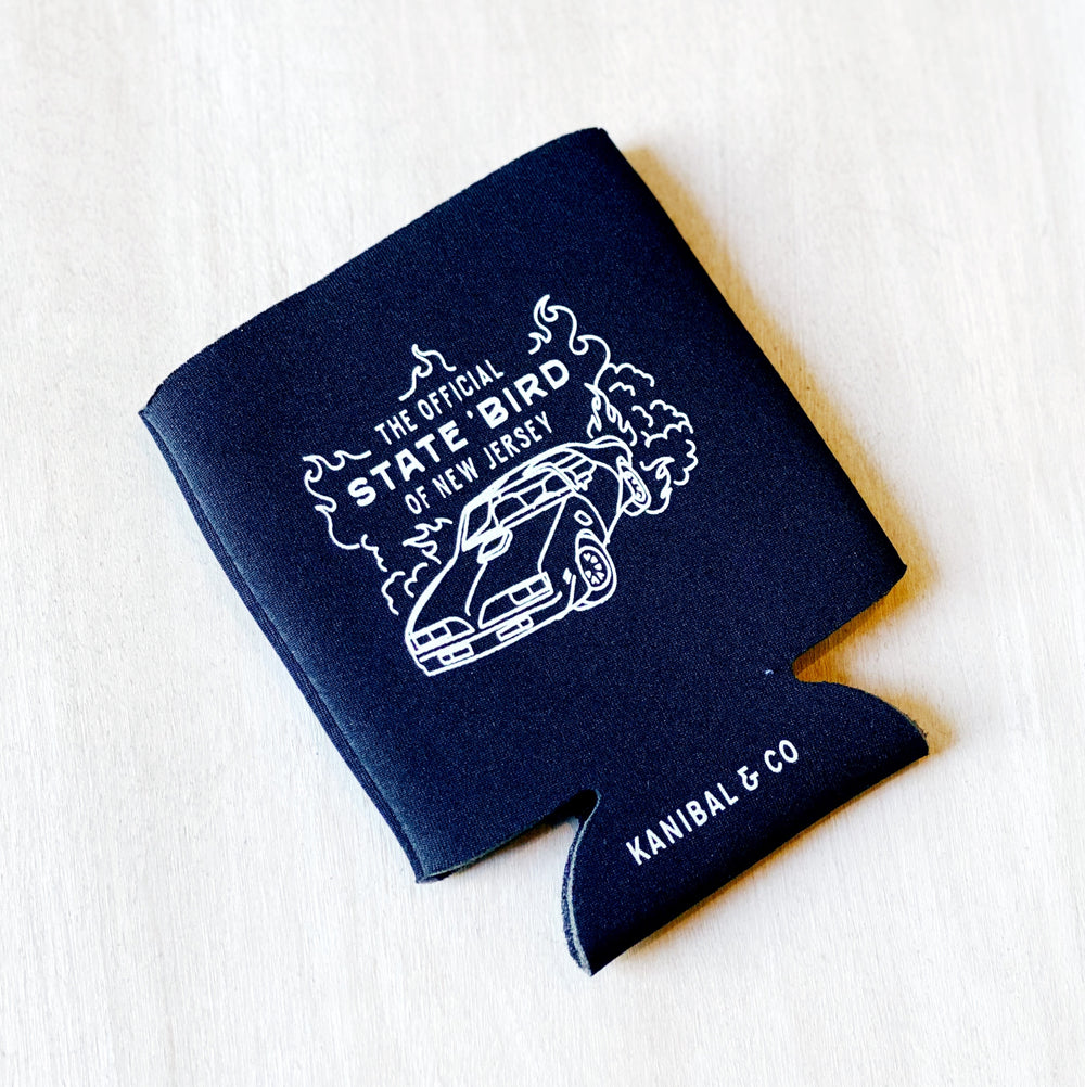 A black beer koozie that has a drawing of a car and flames on it. Within the flames reads "The Official State Bird of New Jersey" in white letters. The bottom of koozie reads "Kanibal & Co."