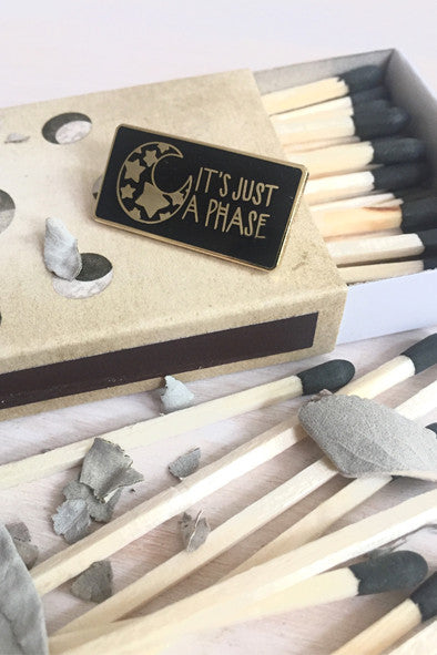 black and gold rectangle pin with illustration of mood with stars inside it on top of a match book
